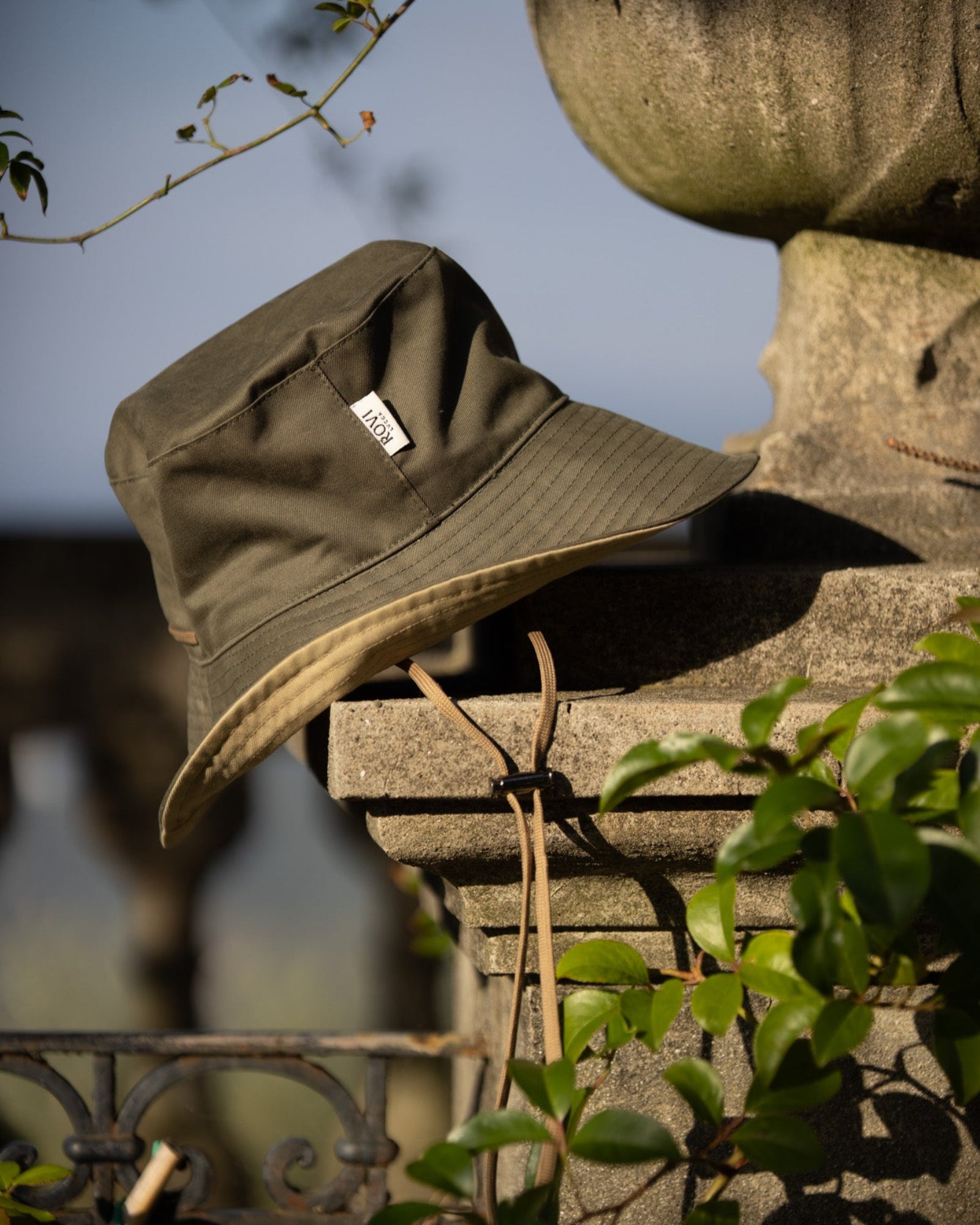 Bucket hat in lovat green and beige cotton twill, styled outdoors in a Tuscan villa garden