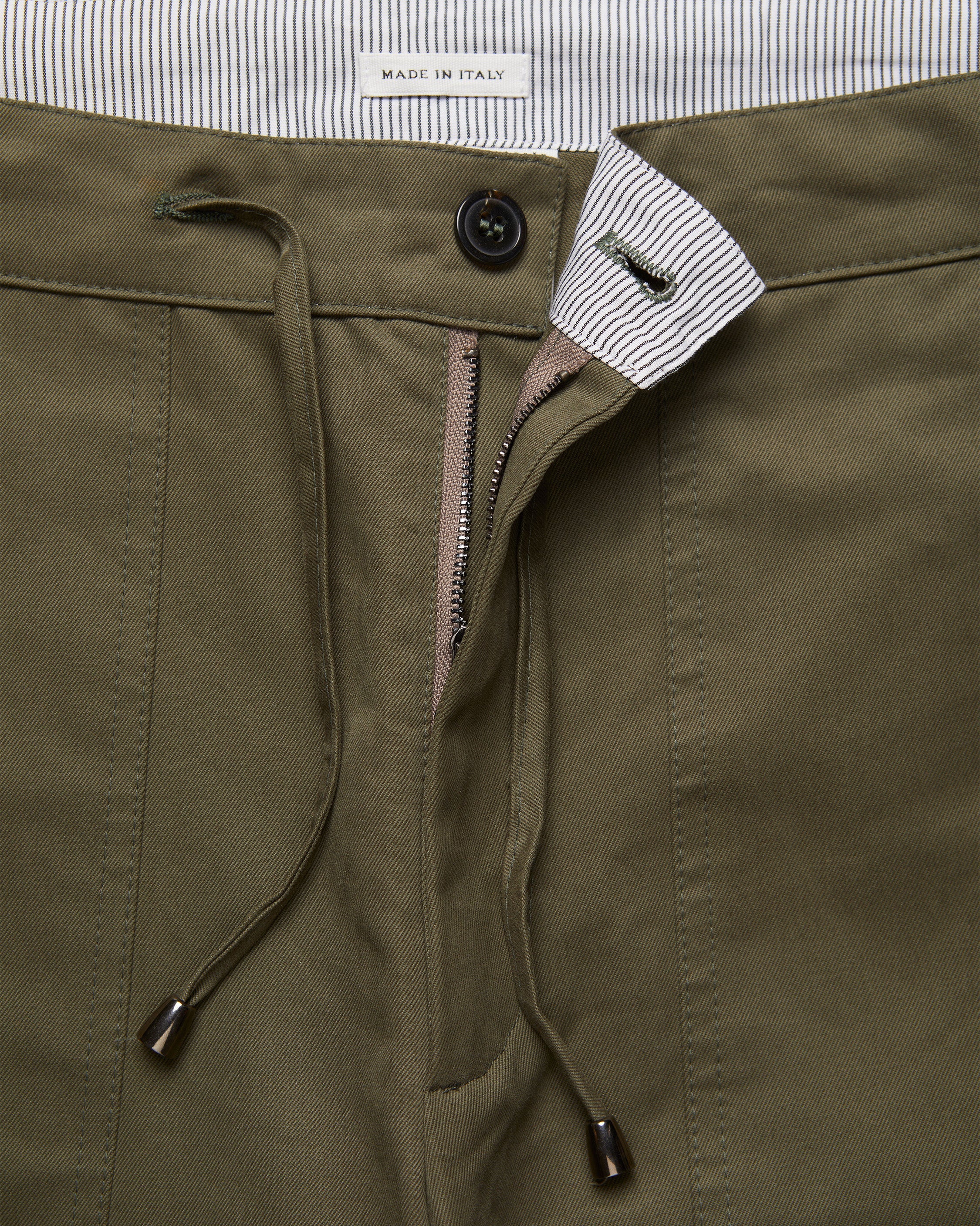 Detail of Lovat Green Utility Trousers showing signature ticking lining, drawstring waist, button and zip closure, crafted in cotton twill, made in Italy.